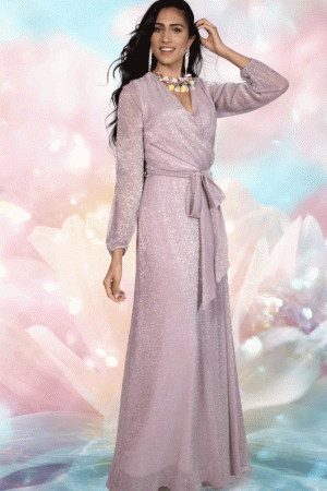 A woman in a shimmering, long-sleeve Frank Lyman - 228212 pale pink gown with a sash at the waist, posing with one hand on her head. The background is ethereal and colorful, resembling a soft-focus floral and light motif. Feeling like she's part of painting number 228212—simply enchanting.