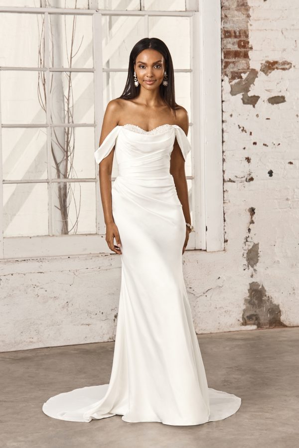 Woman in the Justin Alexander 44388 - Pearl strapless white wedding gown with off-the-shoulder sleeves, standing indoors against a rustic background.