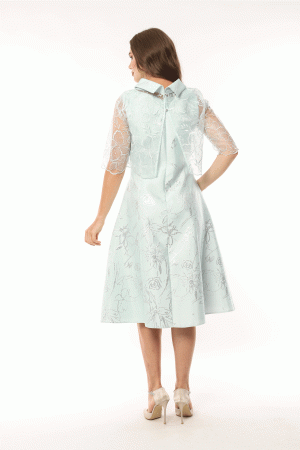A woman in a light blue Lizabella - 2583 dress with lace sleeves and a back bow stands facing away.