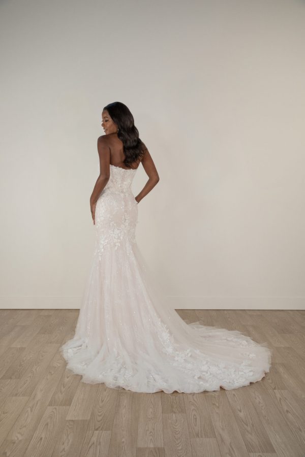 A woman in an elegant Stella York 7924 - Minnie strapless wedding dress with lace details poses gracefully on a wooden floor in a minimalist setting.