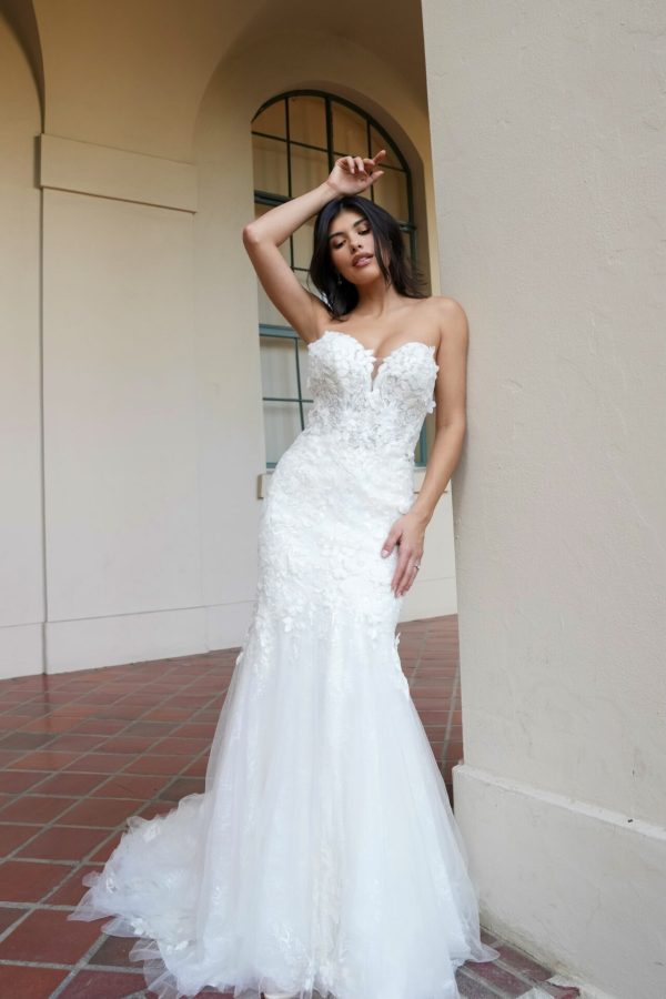 The bride elegantly poses in the Stella York 7924 - Minnie strapless white wedding dress against an arched wall, her hand gently resting on her forehead.