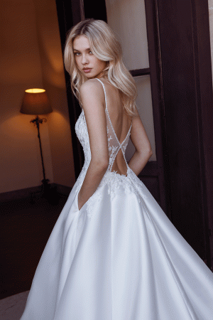 A bride in a stunning Modeca - River wedding dress stands by an open door, glancing over her shoulder, with the serene flow of the river in the background.