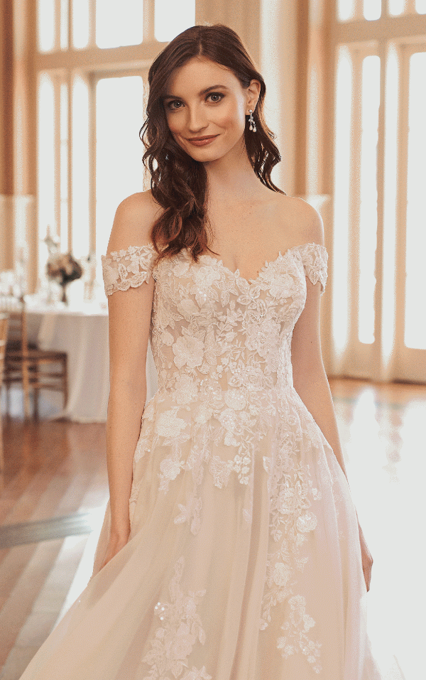 The bride, adorned in a breathtaking Justin Alexander 44312 - Jasmine lace wedding dress, stands gracefully in a bright room with wooden floors and expansive windows.