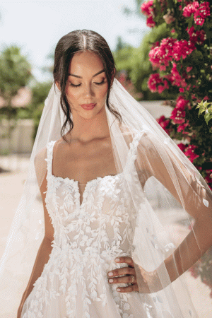 Wearing the Stella York 7965 - Tiger Lilly wedding dress and a veil, the bride stands outdoors, surrounded by a vibrant array of Tiger Lilly flowers.