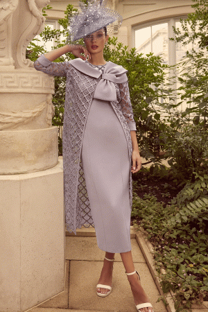 In a garden setting, a woman elegantly poses in the sophisticated style of Veni Infantino 992314, wearing a lavender dress and hat.