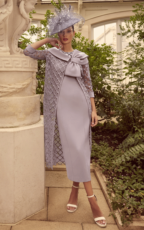 In a garden setting, a woman elegantly poses in the sophisticated style of Veni Infantino 992314, wearing a lavender dress and hat.