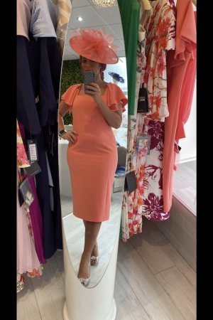 A person wearing a coral Carla Ruiz 199531 dress and hat takes a mirror selfie in a chic clothing store.