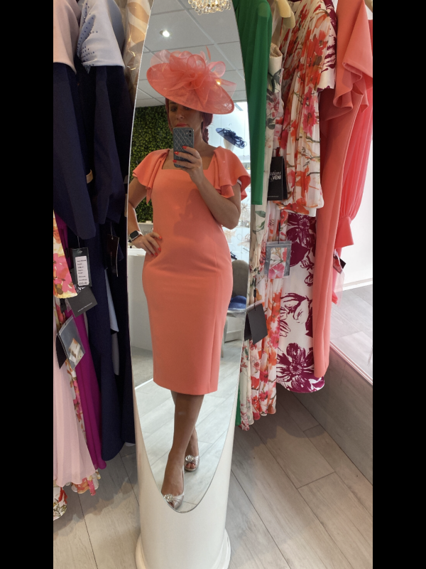 A person wearing a coral Carla Ruiz 199531 dress and hat takes a mirror selfie in a chic clothing store.