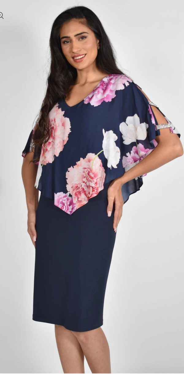 A woman exudes confidence in the Frank Lyman - 222022 creation, donning a navy knee-length dress adorned with a floral-patterned top. Smiling with one hand on her hip, she effortlessly embodies timeless fashion.