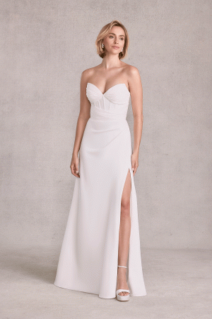 Wearing the stunning Mori Lee 15102 - Sibhon, a strapless white gown featuring a thigh-high slit, the woman stands gracefully against a neutral backdrop, exuding timeless elegance.