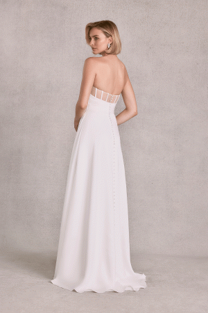 A woman in a strapless Mori Lee 15102 - Sibhon dress with buttons down the back stands gracefully sideways against a gray background.