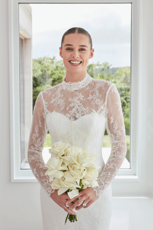 Bride in a Mori Lee 15102 - Sibhon lace wedding dress holding a bouquet of white roses, gracefully standing in front of a window.