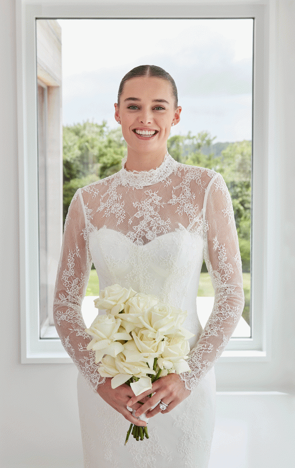 Bride in a Mori Lee 15102 - Sibhon lace wedding dress holding a bouquet of white roses, gracefully standing in front of a window.