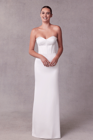 A woman in a stunning strapless Mori Lee 15102 - Sibhon dress stands smiling against a gray background, exuding elegance and grace.