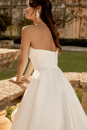 Bride in a strapless white gown leans on a stone railing, elegantly overlooking the 44495 - Inma garden.