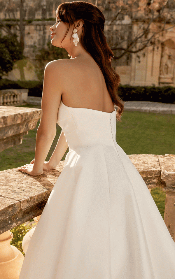 Bride in a strapless white gown leans on a stone railing, elegantly overlooking the 44495 - Inma garden.