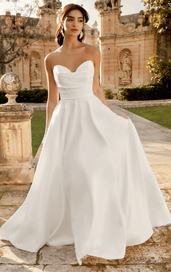 A bride in a strapless white gown poses gracefully outdoors, with the ornate architecture of the Inma (Product 44495) providing an elegant backdrop.