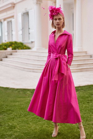 Wearing the Rosa Clara Couture Club - 9GM8, a member dazzles in vibrant pink with a matching hat, gracefully posed on the grass before a grand white building with columns.