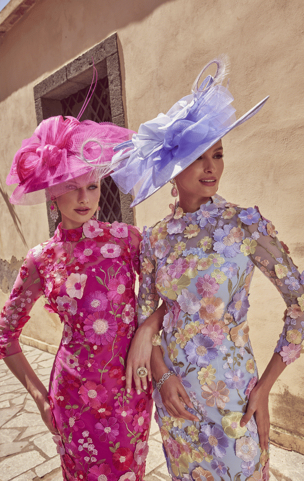 Two women in Veni Infantino 992445 floral dresses and large hats pose elegantly outside a building.