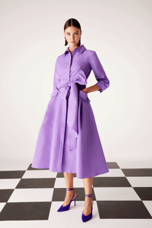 A woman in a chic Carla Ruiz - 51547 purple dress and heels stands elegantly on a black and white checkered floor.