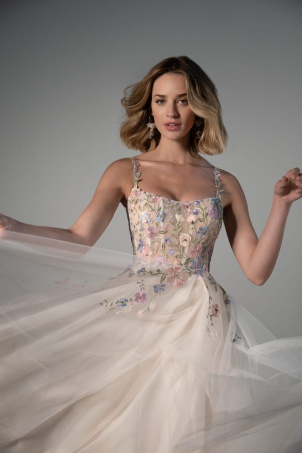 Leilani twirls gracefully in the Stella York 8063 gown with floral embroidery, her dress's delicate motion exuding elegance against a grey background.