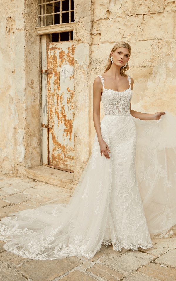 Bride in a Justin Alexander 44482 - Marylise lace wedding dress with train, standing by an aged stone wall and rusty door.