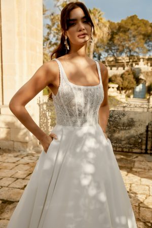 Wearing the Sincerity 44493 - Vivienne white wedding dress adorned with lace details, the person stands elegantly on a stone path, framed by trees and an archway.