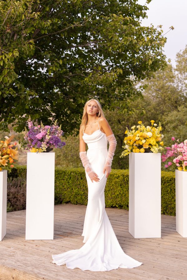 Bride Brooke, wearing the elegant Stella York 7831 gown, poses outdoors next to exquisite floral arrangements on white pedestals.