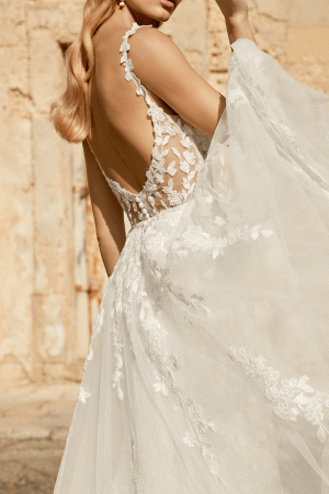Bride in a Justin Alexander 44482 - Marylise lace wedding dress, featuring an open back and delicate floral details, elegantly posed against a rustic stone wall.
