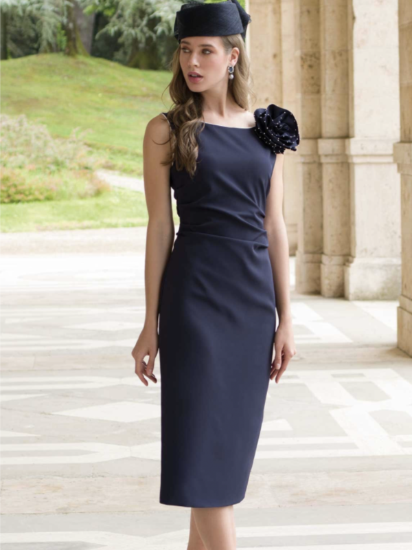 Michaela Louisa's ONLINE PURCHASE ONLY style 9020 showcases a woman in a chic dark blue dress and hat, posed elegantly on a marble floor in an open-air setting. The perfect mix of sophistication and modern flair.