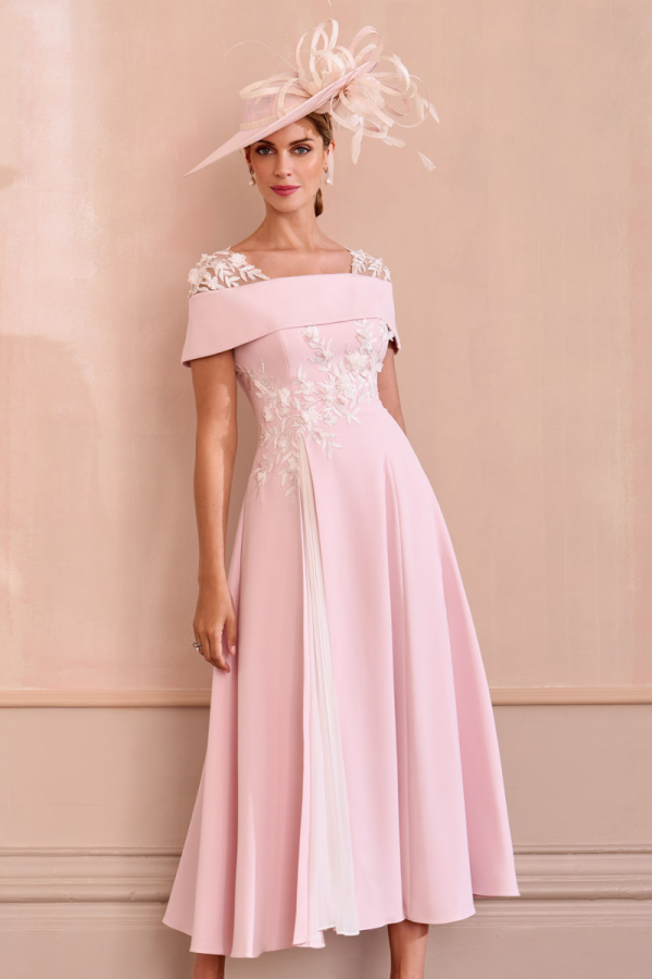 A woman poses against a beige wall in a John Charles - 66625, an elegant pink midi dress adorned with floral embroidery, paired with a large matching hat.