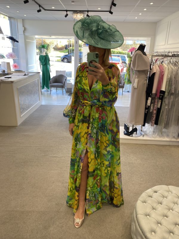 Amidst the elegant clothing racks, a vibrant scene unfolds as a person captures a selfie while wearing a Carla Ruiz - 51662 floral dress and wide-brim hat.