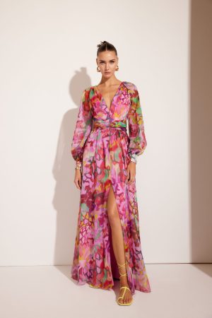 The person is wearing the vibrant Carla Ruiz - 51662 floral dress with a thigh-high slit, standing against a plain background.