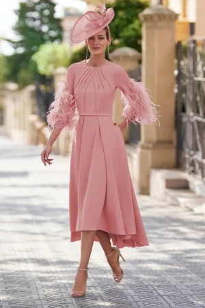 Woman wearing the Rosa Clara - 9G1N2 pink midi dress with feathered sleeves and a matching hat, walking outdoors on a sunny day.