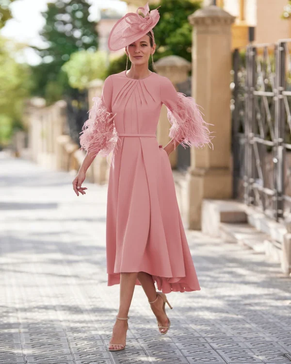 Woman wearing the Rosa Clara - 9G1N2 pink midi dress with feathered sleeves and a matching hat, walking outdoors on a sunny day.