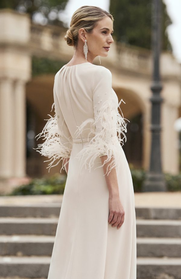 Woman in a chic white Rosa Clara - 8G145 wedding dress with feathered sleeves, standing outdoors and gazing to the side.
