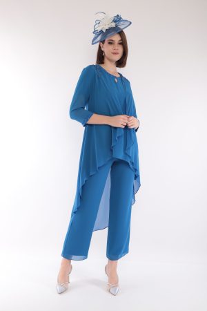 A woman models the elegant Lizabella 7299, a blue outfit with white accents and matching hat, standing against a plain white background.