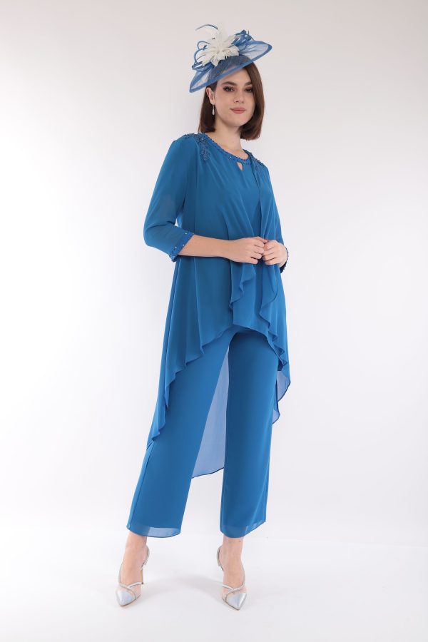 A woman models the elegant Lizabella 7299, a blue outfit with white accents and matching hat, standing against a plain white background.