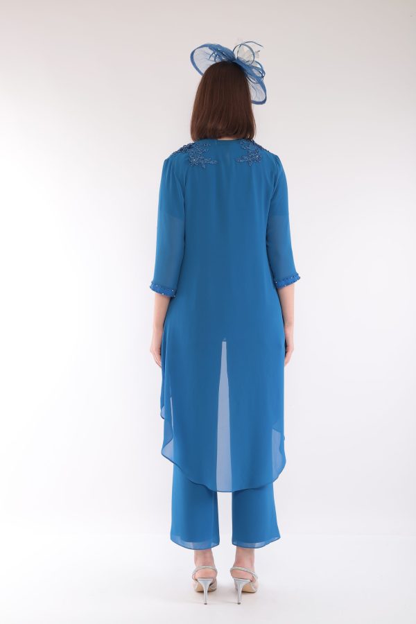A woman faces away against a white background, wearing a blue Lizabella 7299 outfit with a matching hat.