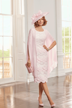 A woman stands in a bright, elegant room wearing the Condici - 71125 pale pink lace mother of the bride dress, paired with a matching hat and heels.