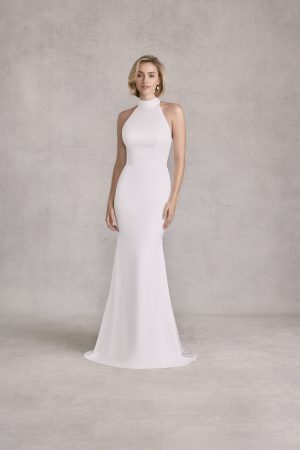 Woman in the Morilee 15101 - Sandi sleeveless, high-neck, floor-length white dress stands against a plain light gray background.