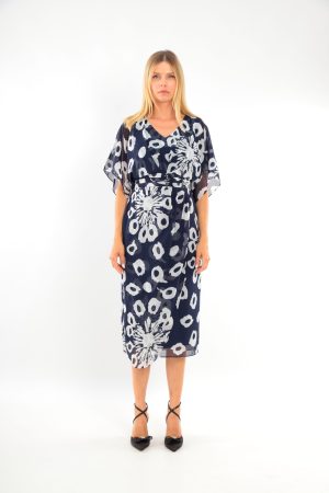 Woman in a navy blue dress with white floral patterns, standing against a plain white background.