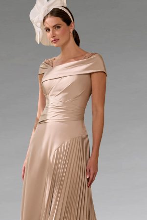Woman in an elegant beige John Charles - 66661A dress with pleats and an off-shoulder neckline, styled with a large white fascinator.