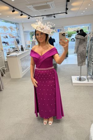 Woman in a Veni Infantino - 992571 magenta off-shoulder dress and white fascinator taking a mirror selfie in a boutique.