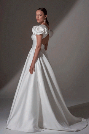 Woman in an elegant white gown with puffed sleeves and a long skirt, posing against a neutral background.