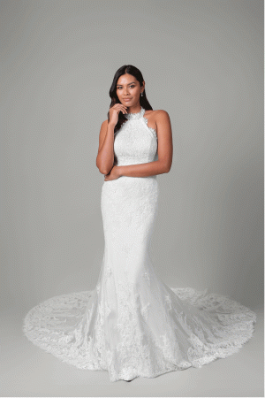 A woman wears the Justin Alexander - Reese, a sleeveless lace wedding gown with a long train, standing against a plain grey background.