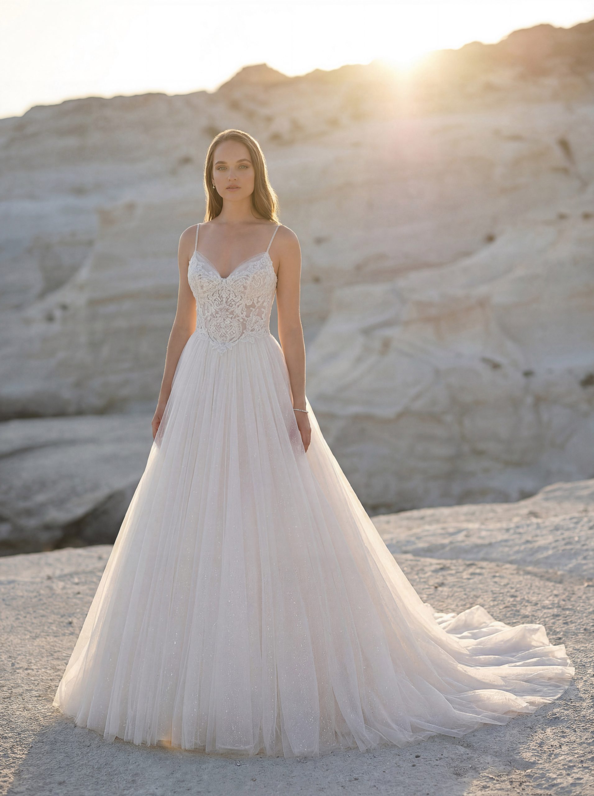 A woman wearing a white wedding dress stands on the rocky Tuscan landscape at sunset, featuring product 1050027 - Toscana.